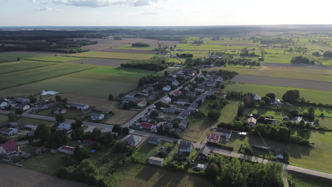 Aerial dolly in view of Szumsk village in Poland, surrounded by rural green and cereal fields. Scenic drone flight