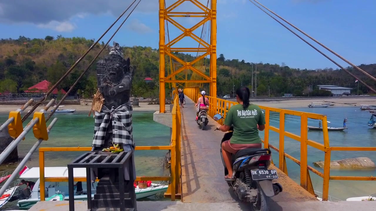 Pengambilan gambar miring penduduk lokal Indonesia mengendarai sepeda motor di Jembatan Kuning di Nusa Lembongan, sebuah pulau yang terletak di tenggara Bali, Indonesia