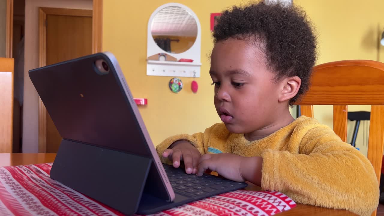 niño negro de 3 años enfocado mientras juega con un ipad sentado en casa
