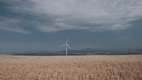 una turbina eólica girando en un campo de trigo con cielos azules nubes y montañas