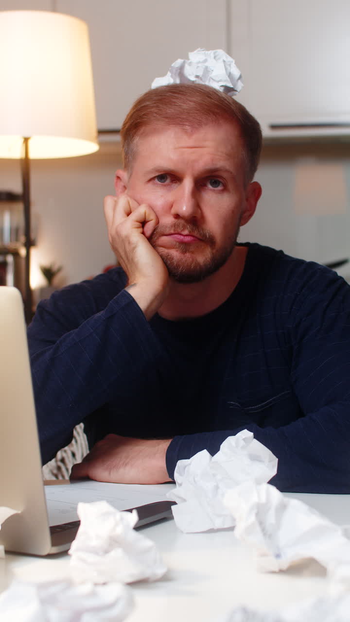 Young man fights creative block writes ideas for project with crumpled paper critique mood at night