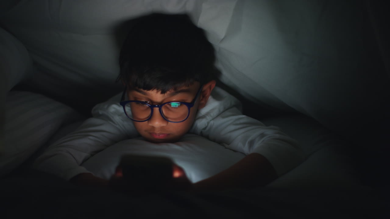 Close Up Of Young Boy In Bedroom At Home Using Mobile Phone To Text Message Under Covers Or Duvet At Night 6