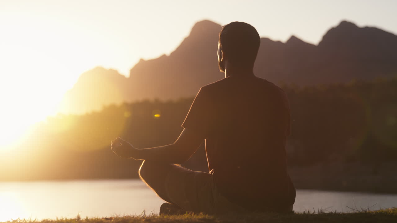 hombre meditando haciendo yoga junto a un hermoso lago y montañas al atardecer