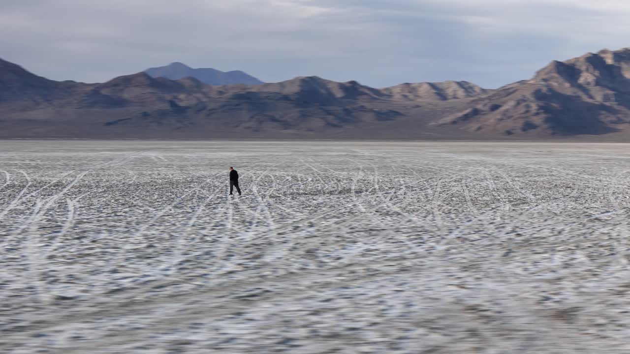 Ripresa aerea di un uomo che cammina da solo nel terreno arido delle Bonneville Salt Flats, Utah ISA