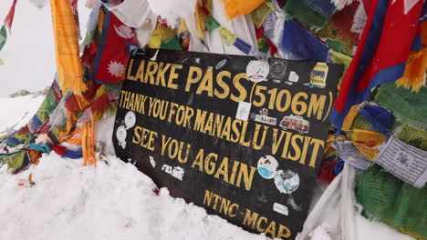 sign and flags at the larke pass on the manaslu circuit trek, nepal