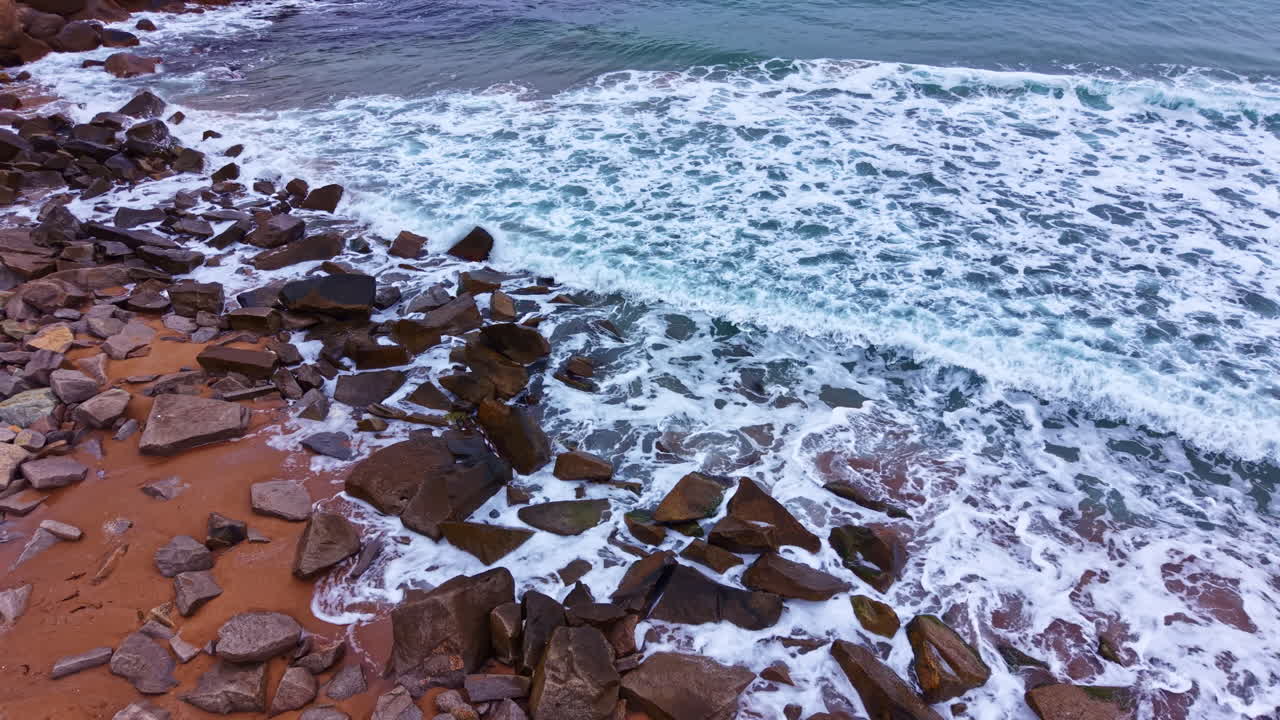 Le onde si infrangono contro le rocce su una spiaggia sabbiosa con l'acqua dell'oceano che si estende fino all'orizzonte vicino a una zona costiera a mezzogiorno.