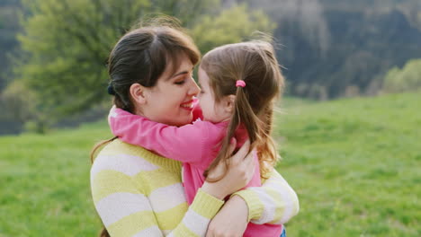 Kleines-Mädchen-Umarmt-Mit-Ihrer-Jungen-Mutter-Im-Frühlingsgarten