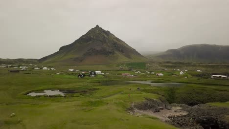 Luftaufnahmen-Von-Bergen-über-Holzhäusern-Und-See-Während-Des-Bewölkten-Sommers-In-Hellnar,-Halbinsel-Snaefellsness,-Island