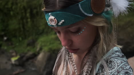 mujer con una cinta para la cabeza boho y un traje de plumas junto a una cascada