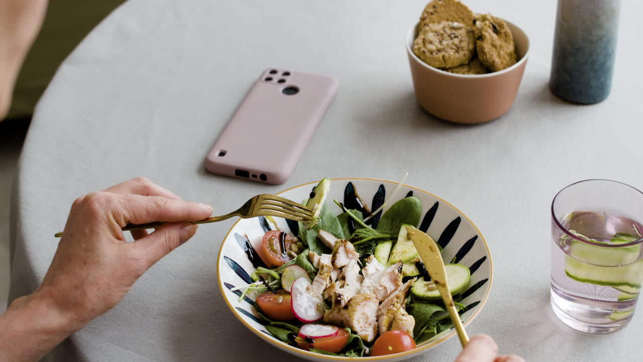 Person eating a healthy salad with a smartphone and water on the table