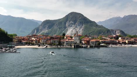 Low-Dolly-Aufnahme-Einer-Wunderschönen-Villa-Am-Ende-Eines-Sees-Mit-Majestätisch-Aufragenden-Bergen-Und-Einem-Boot,-Das-Am-Ruhigen-Strand-Anlegt