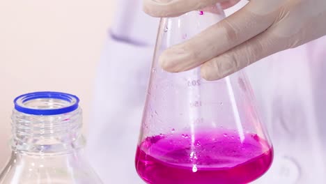a scientist stirs a vibrant pink solution in a conical flask using a pipette.