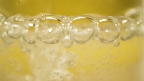 Bubbles-burst,-extreme-close-up-sparkling-fizzy-water-with-yellow-background