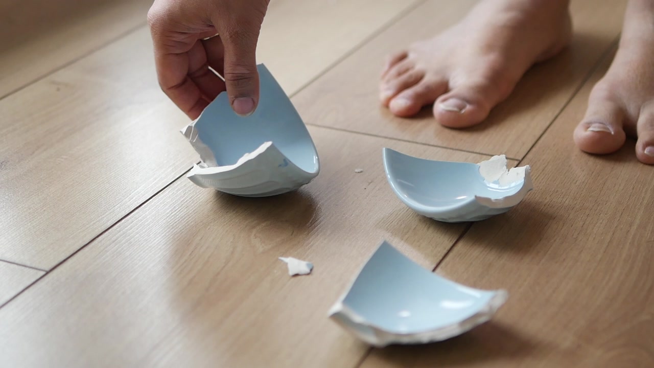 Person's Hand Picks Up Pieces of a Broken Ceramic Dish from the Floor