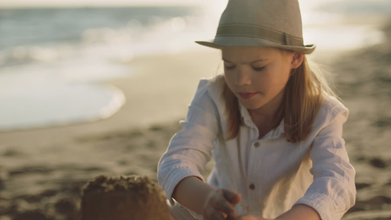 niña construyendo un castillo de arena en la playa al atardecer