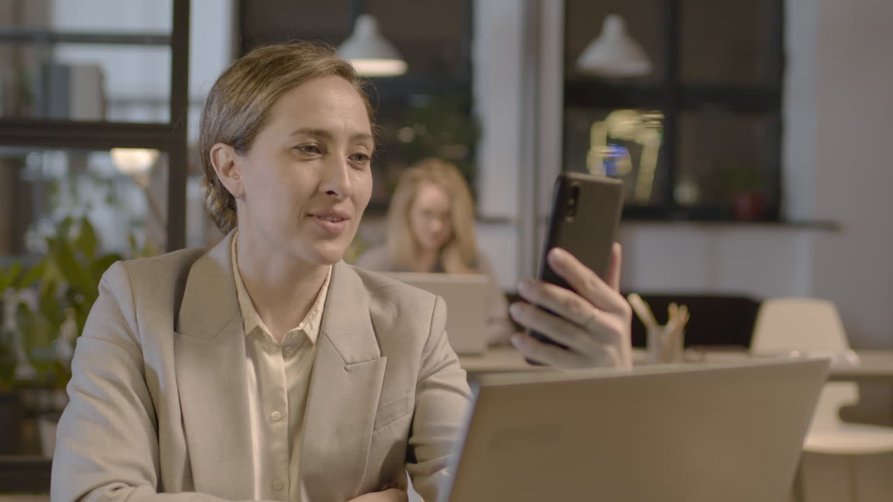 mujer de negocios sonriente que tiene una videollamada con el teléfono móvil mientras trabaja en la oficina 2