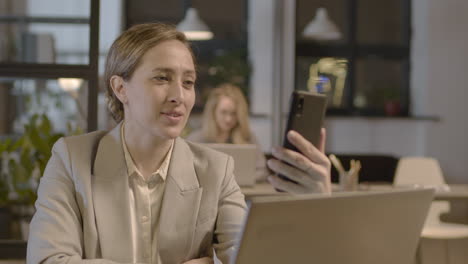 Smiling-Businesswoman-Having-A-Video-Call-With-The-Mobile-Phone-While-Working-In-The-Office-2