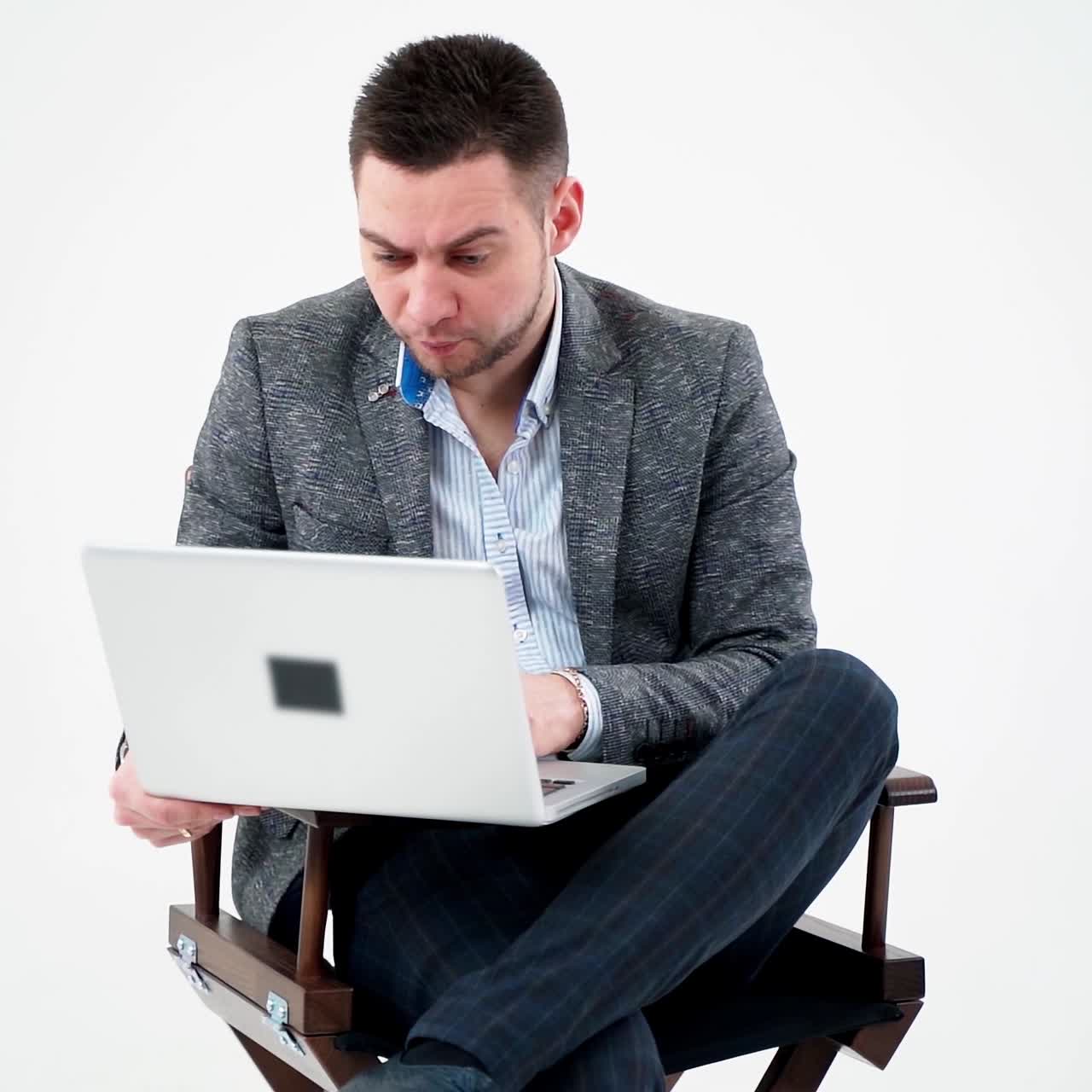 Grieved businessman looking into the laptop. Pensive male freelancer working on a modern gadget while sitting alone on white background.