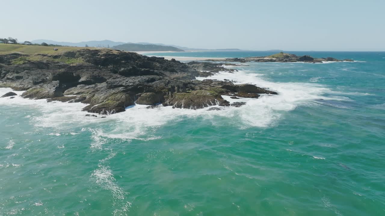 Clip di drone che mostra un pittoresco promontorio roccioso australiano e un oceano blu chiaro con onde di schiuma bianca.