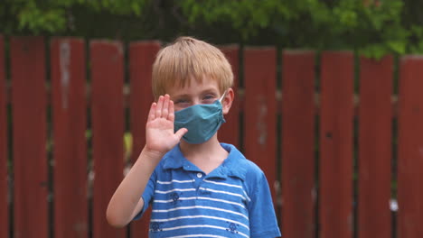 cute little boy waving while wearing a protective face mask