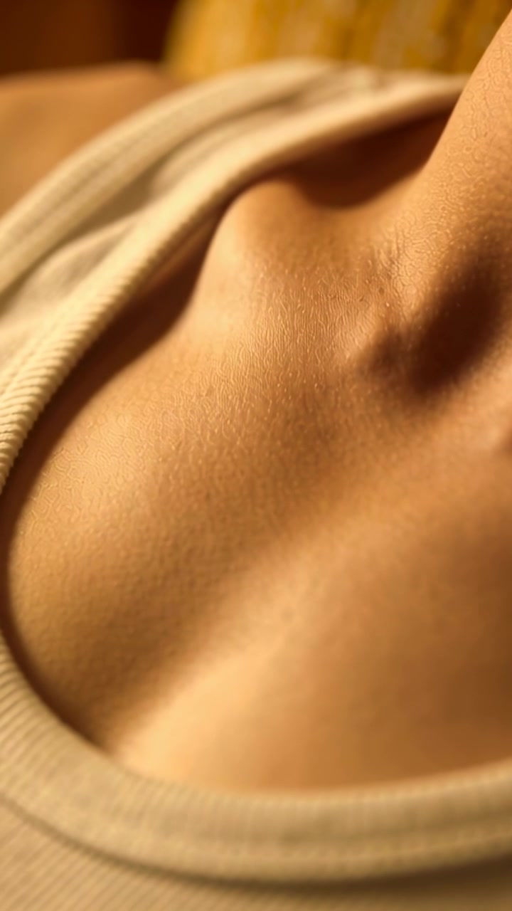 Video verticale: Torso femminile che respira, muovendosi leggermente sul letto, rivelando una canotta a costine e un cuscino.
