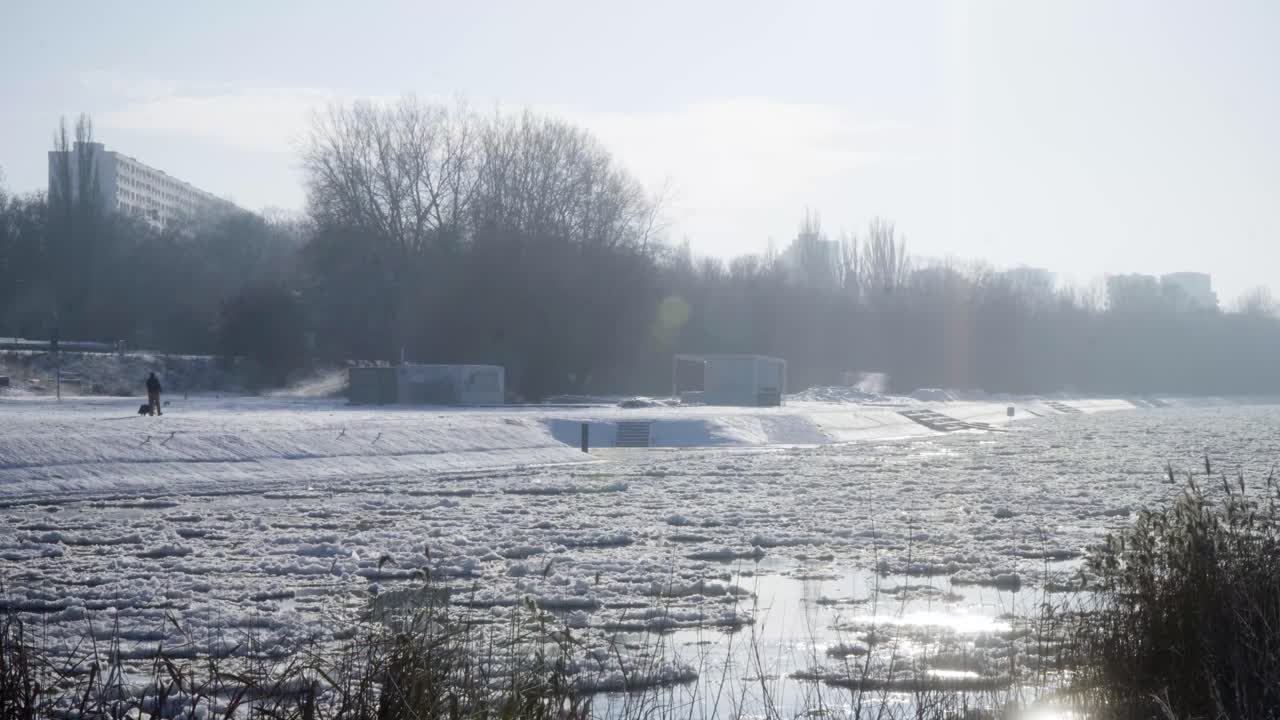겨울 동안 백그라운드에서 평평한 블록과 함께 얼음 floes와 함께 rozen 강 옆에 개와 함께 산책하는 남자