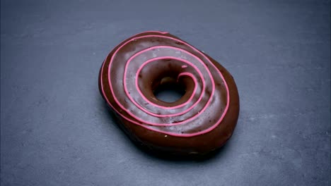 close-up shot of glazed brown donut spinning around and bitten on gray table background.