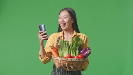 woman holding basket of vegetables and using smartphone