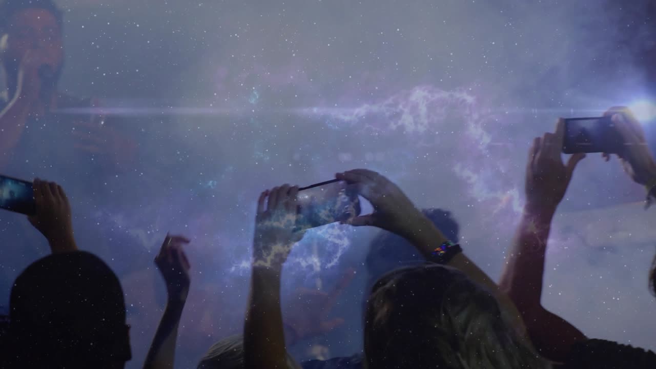 Concert-goers raising phones, filming nebula as burst of light appearing on stage causing cheering