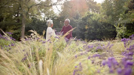 Senior-biracial-couple-dancing-together-in-sunny-garden,-unaltered,-copy-space,-in-slow-motion