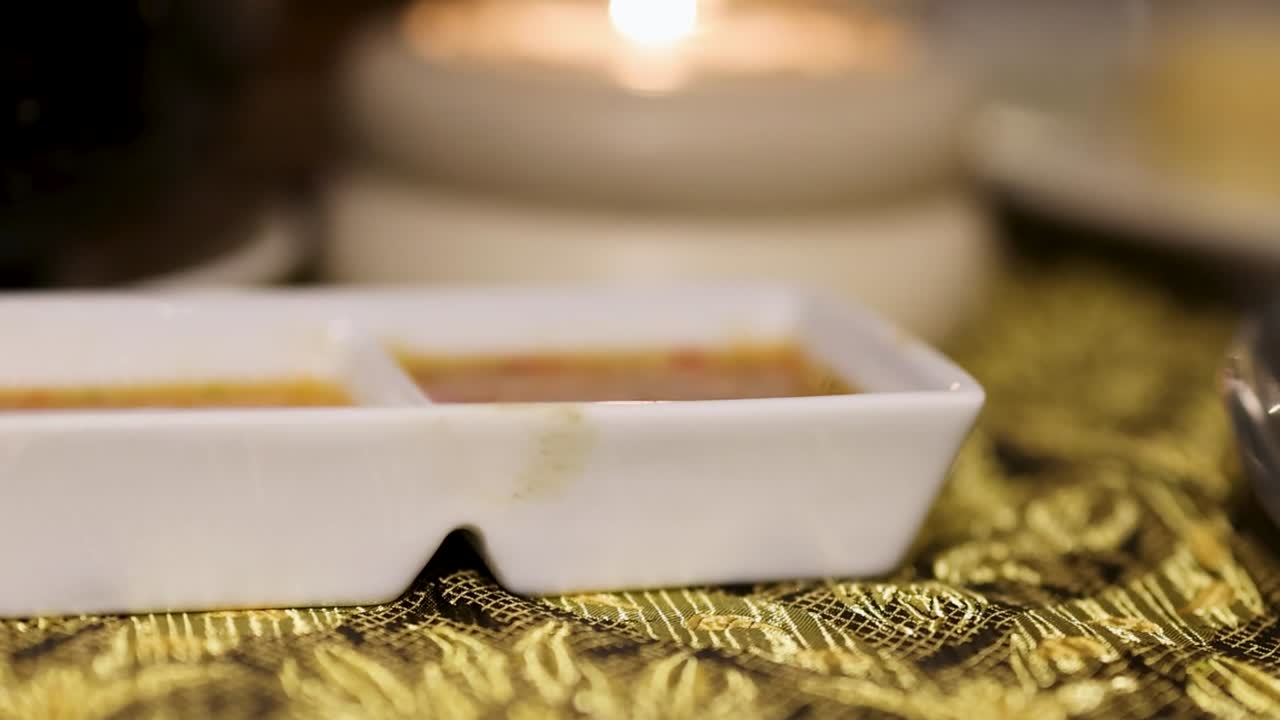 A detailed view of a white sauce dish on a decorative fabric, illuminated by soft candlelight.