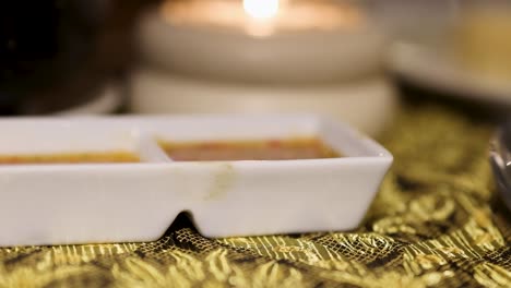 a detailed view of a white sauce dish on a decorative fabric, illuminated by soft candlelight.