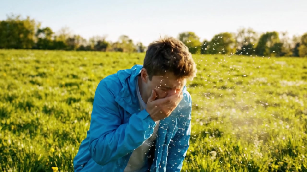 En ung mand i en blå jakke går gennem en frodig grøn mark, fanger rolige øjeblikke i naturen midt i strålende solskin og klar himmel