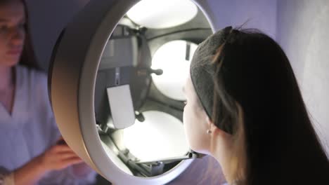 cosmetologist performing facial examination under lamp