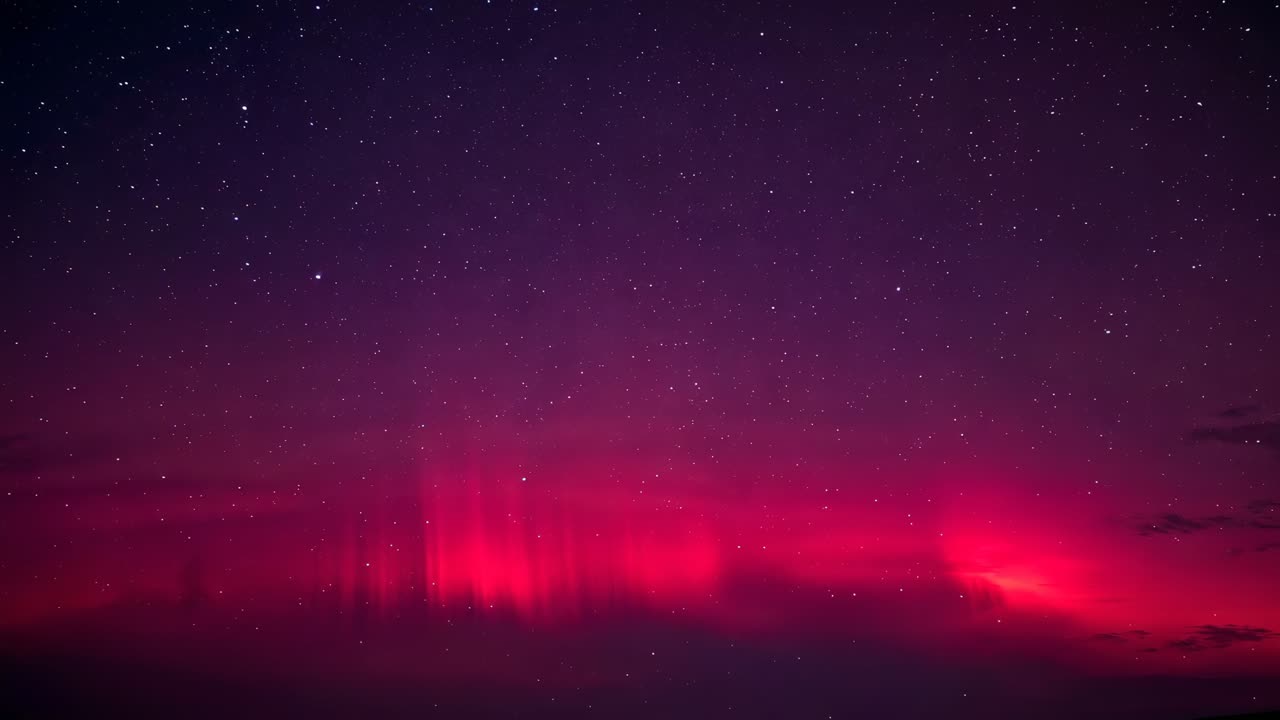 Brightening pink aurora band stretching across starry sky, sending vertical rays above dark horizon