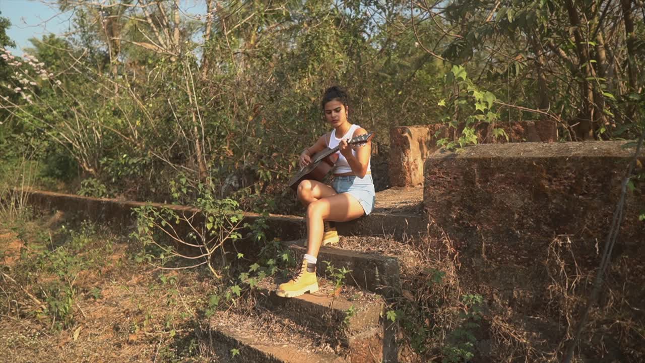 mujer joven haciendo un picnic en la naturaleza y tocando la guitarra - una niña tocando la guitarra sentada sola en las escaleras