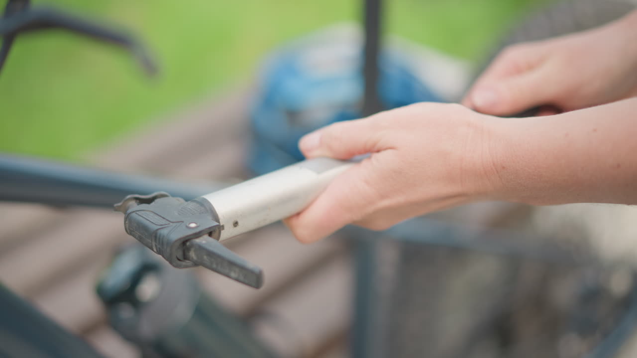 Gros plan sur une femme préparant une pompe portable pour gonfler un pneu de vélo dans un parc, les mains attachant l’adaptateur de valve, fond vert ensoleillé, casque de sécurité sur un banc, routine active de navetteur, lecture claire de la jauge