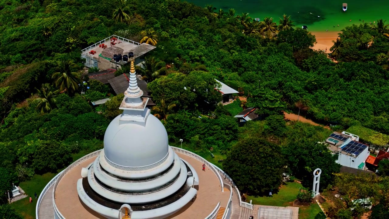 La Pagoda Bianca della Pace Giapponese corona la collina di Rumassala mentre un drone sorvola una foresta lussureggiante verso la piccola baia sottostante