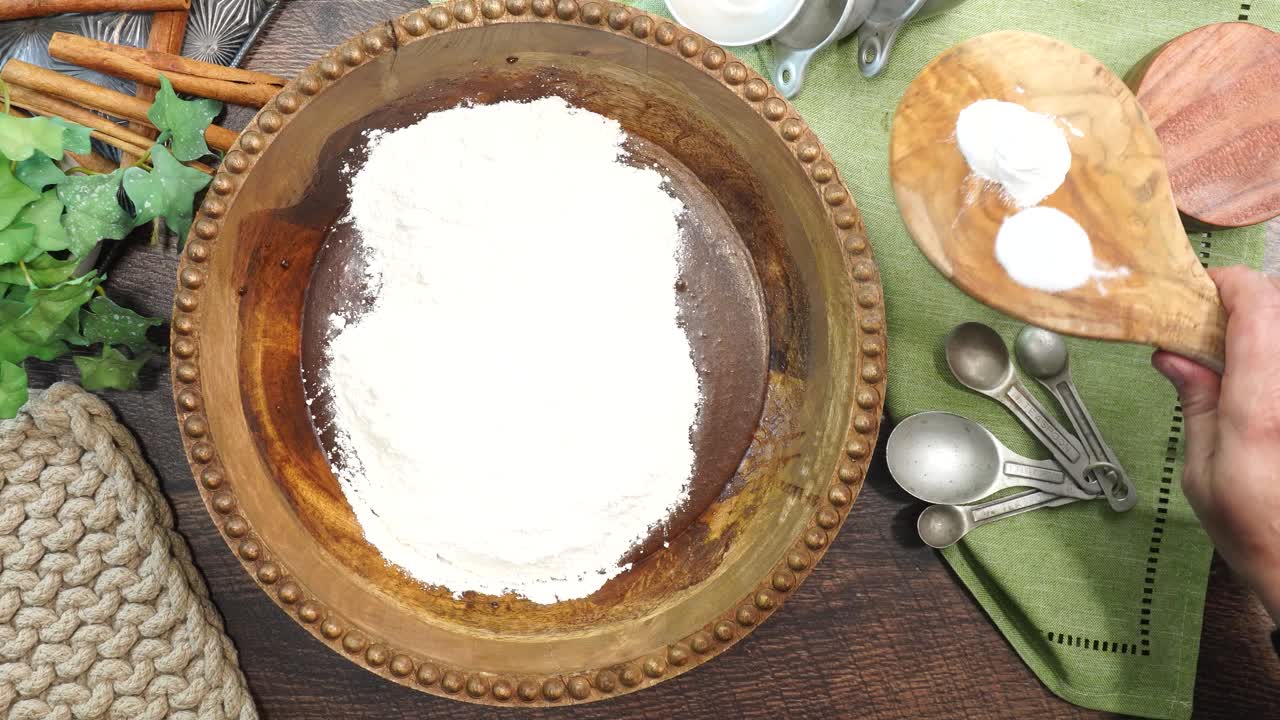 Baking a carrot cake loaf with cream cheese icing and topped with roasted salted pecans. Making a Autumn dessert with carrots, flour, sugar, nuts and frosting. Mixing in baking powder and baking soda.