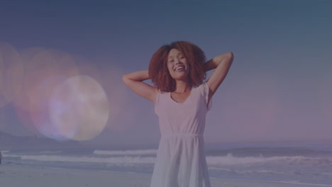 Animation of light spots moving over happy biracial woman with arms wide on beach