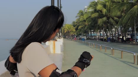 asian female puts on wrist guard for safe inline skating at the coastal park in thailand