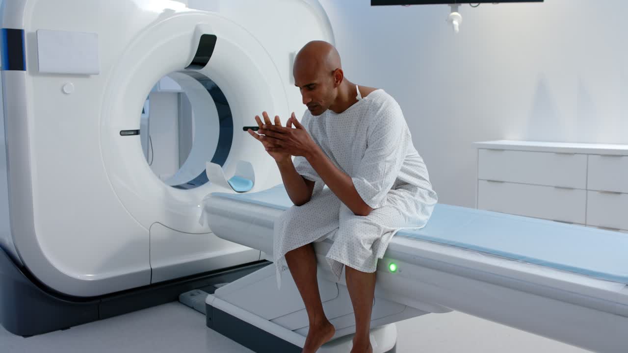 Uomo afroamericano in camice bianco seduto al tavolo dello scanner, luce verde che indica la preparazione per la scansione