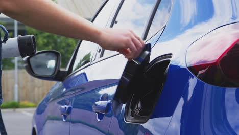 mujer separando el cable de carga de un coche eléctrico ecológico de cero emisiones al aire libre