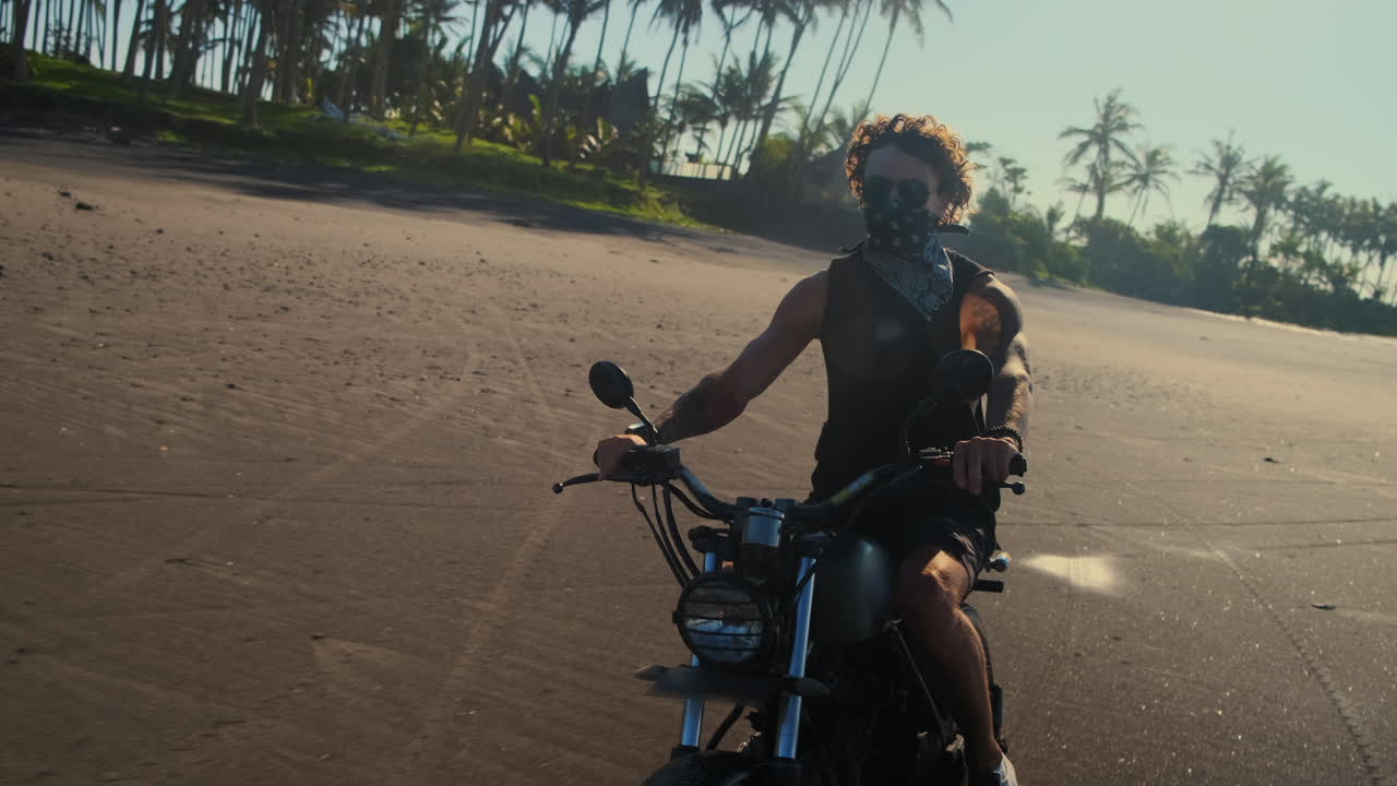 Man riding a motorcycle on a black sand beach at sunset