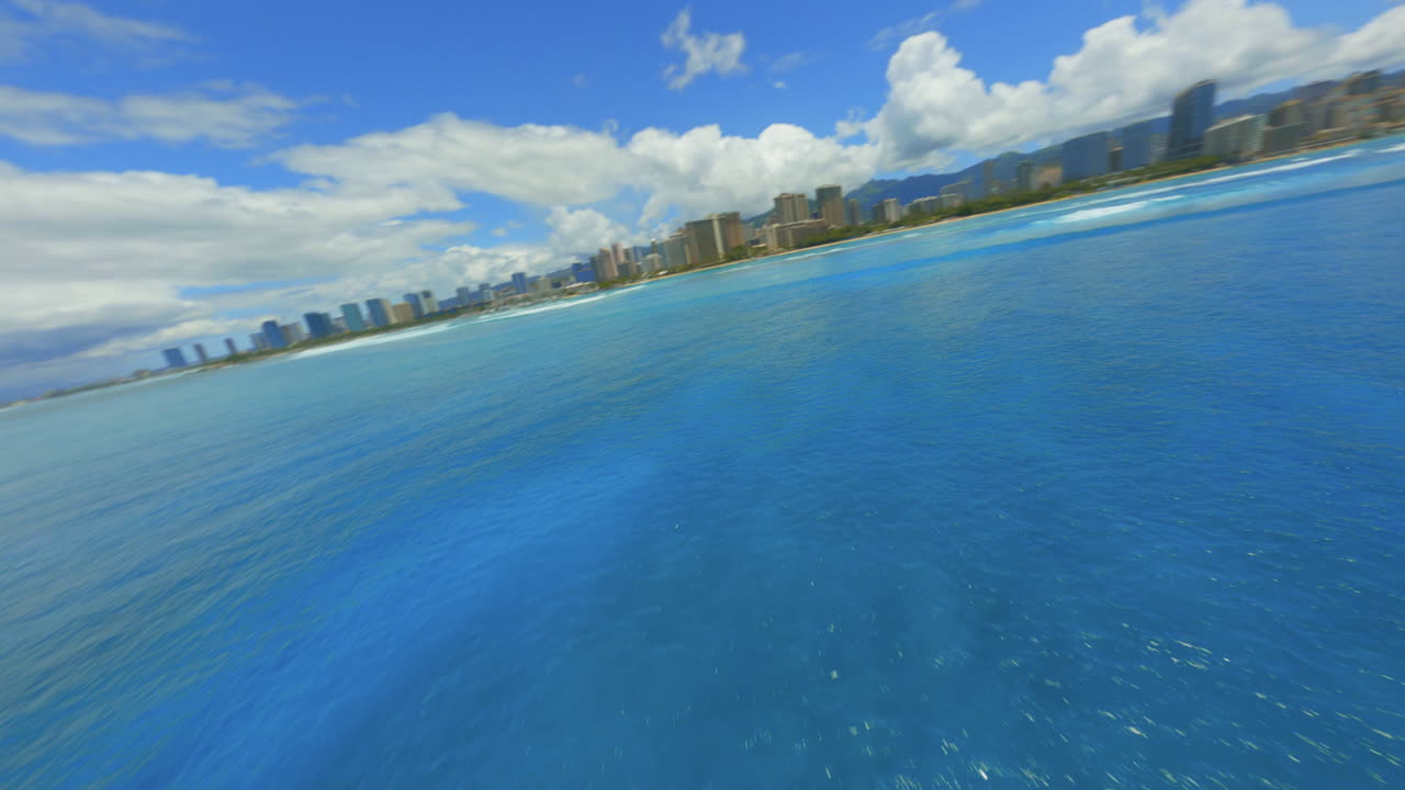 호놀루를 향해 날아가는 fpv 드론이 밝은 파란색 태평양과 와이키키 해변을 향해 도시 스카이 라인을 향해 날고 있습니다.