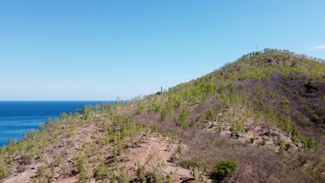 Vista-Aérea-En-Aumento-De-La-Estatua-De-Cristo-Rei,-Un-Hito-Turístico,-En-La-Distancia-Con-Colinas-Y-Montañas-De-Dili,-Timor-leste-En-El-Sudeste-Asiático