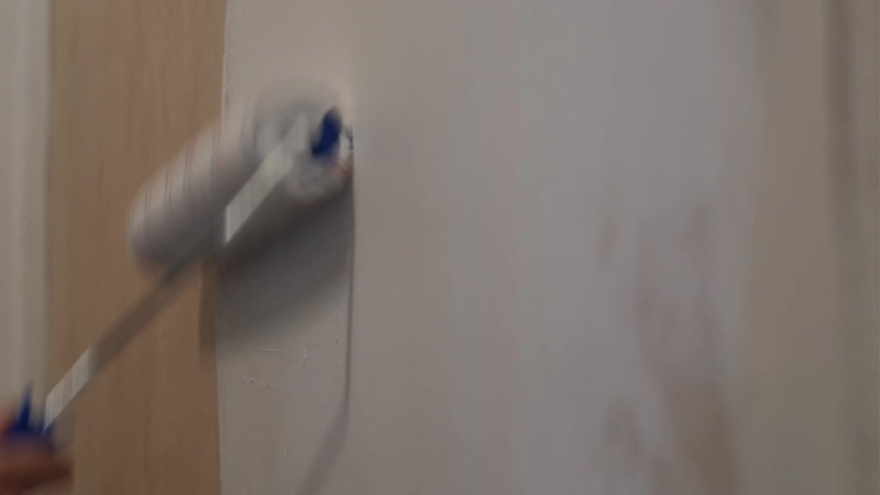 Close-up shot of a paint roller applying white paint on an interior wall during indoor renovation work