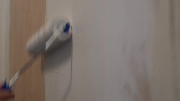 Close-up shot of a paint roller applying white paint on an interior wall during indoor renovation work