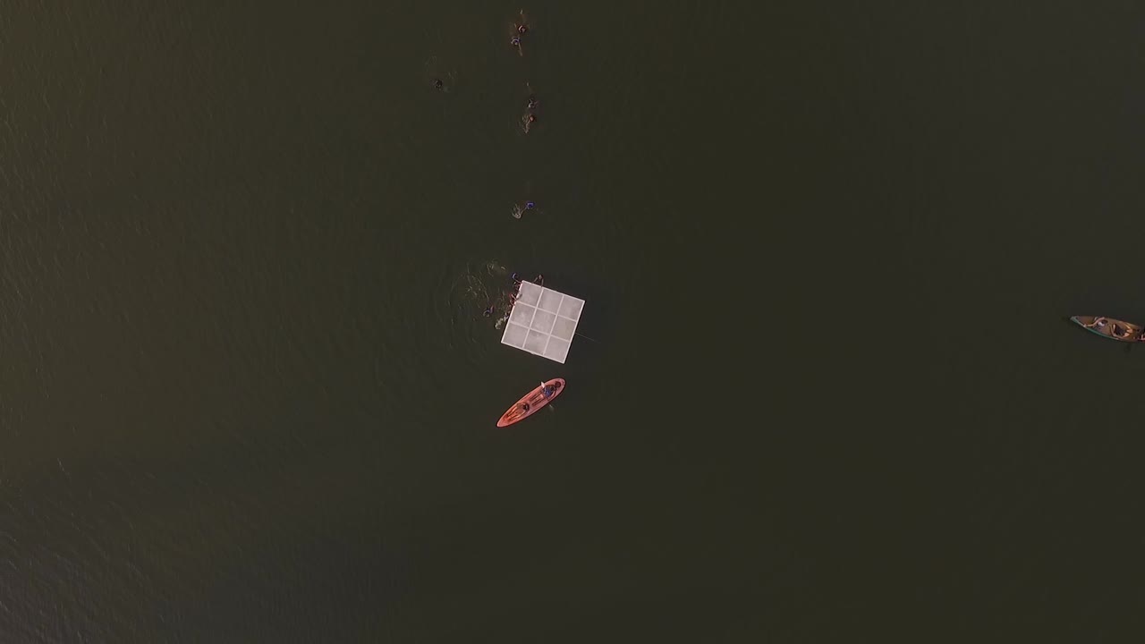 vista aérea de niños divirtiéndose nadando en la plataforma de un lago en un campamento de verano, con un kayak y una canoa flotando en el lago