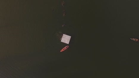 Aerial view of kids having fun swimming to a lake's platform in a summer camp, with a kayak and canoe floating in the lake